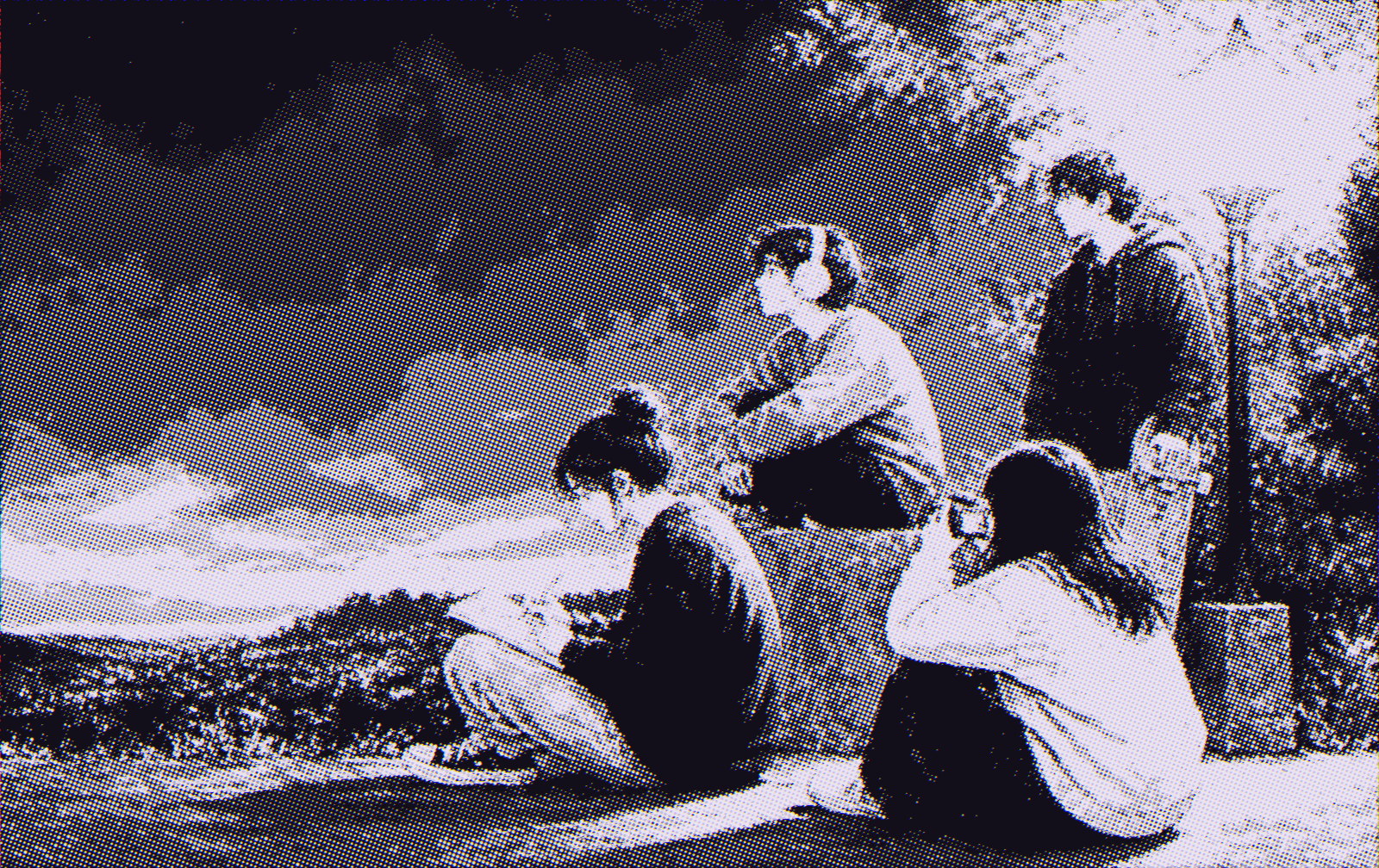 Four teenagers sitting together at dusk, one drawing, one listening to music, one with a skateboard, one taking a photo